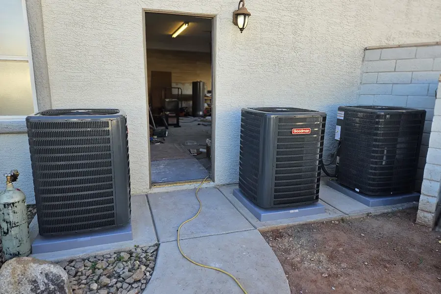 Three air conditioner condensers on concrete pads behind a home