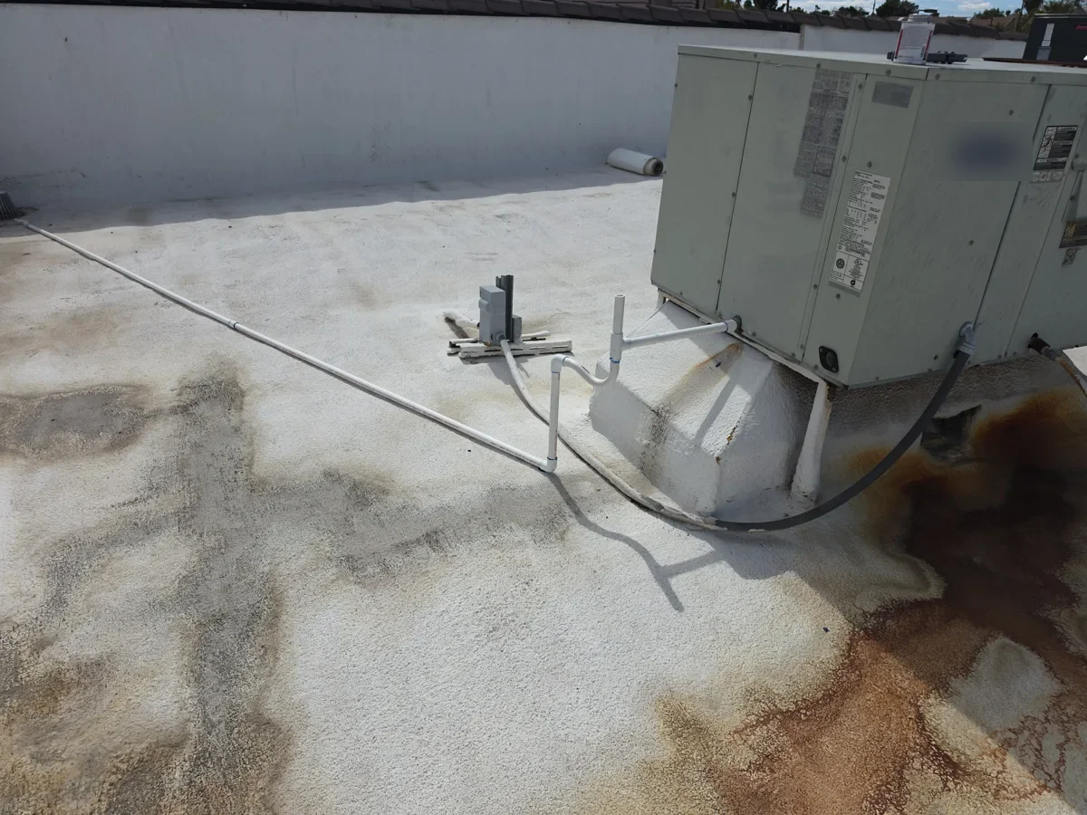 Rooftop package HVAC unit on a coated flat roof with conduit and condensate piping
